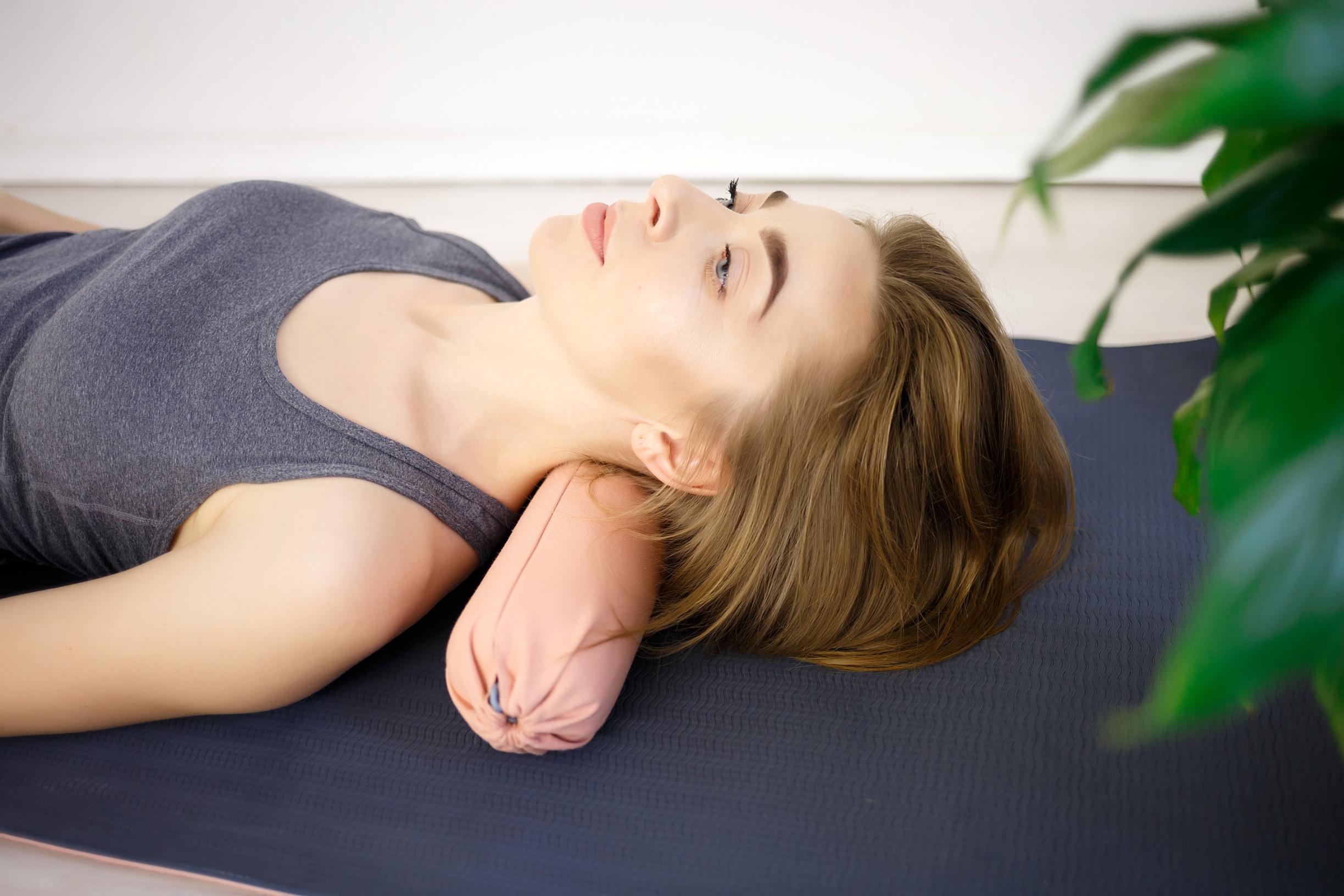 En kvinne slapper av på en yogamatte med lukkede øyne, og bruker en pute for støtte.